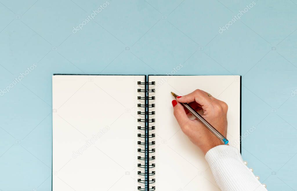 Girl hand handwriting in a notebook. Blue pastel background of workspace, copy space, flat lay.