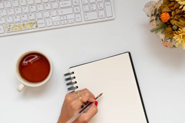 Evde boş bir deftere el yazısı yazan bir kız. Çalışma alanının düz konumu