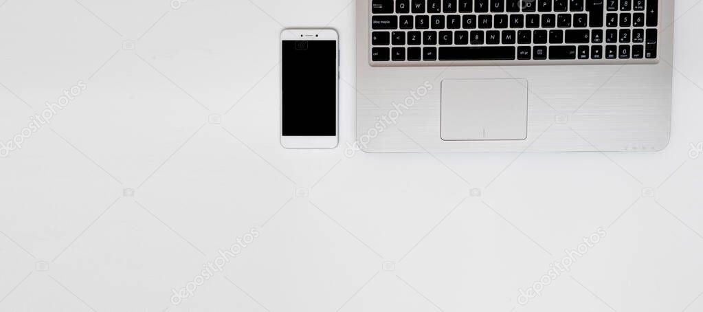 Smartphone mock-up with laptop. Banner with white copy space perfect for blogging. White surface of workplace, flat lay