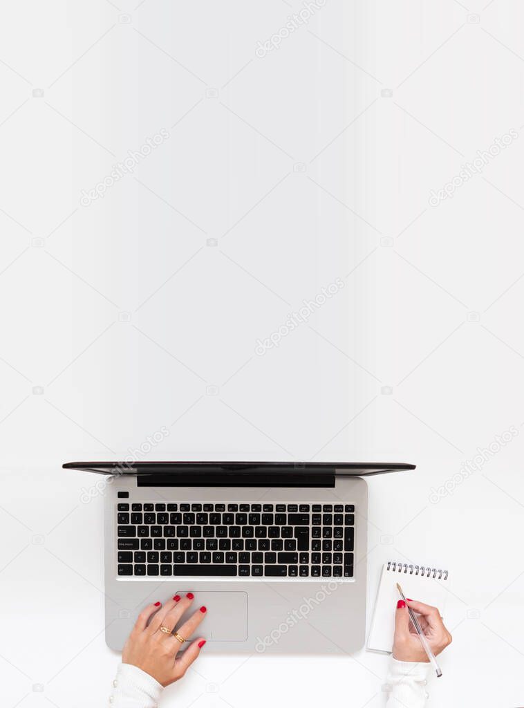 Vertical shot of girl hands typing and writing notes. Top view, flat lay, girl working at home while telecommuting with copy space