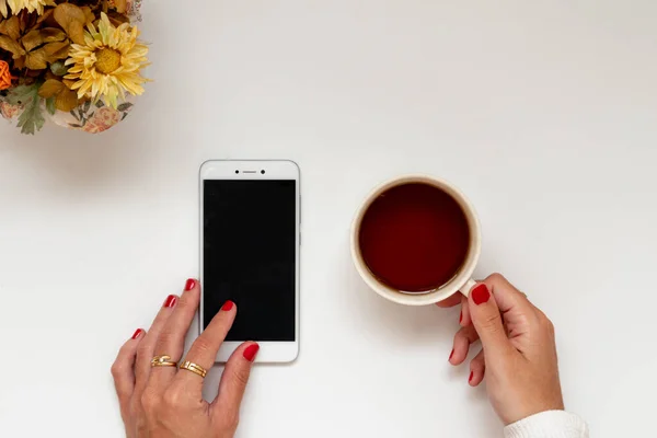 Girl hands with tea and phone in a surface, cozy home scene in quarantine. Flat lay, top view