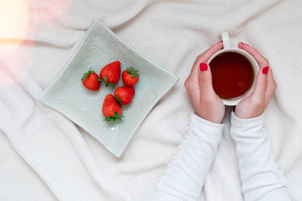 Girl hands around a tea cup with tasty strawberries. Cozy and comfortable scene at home