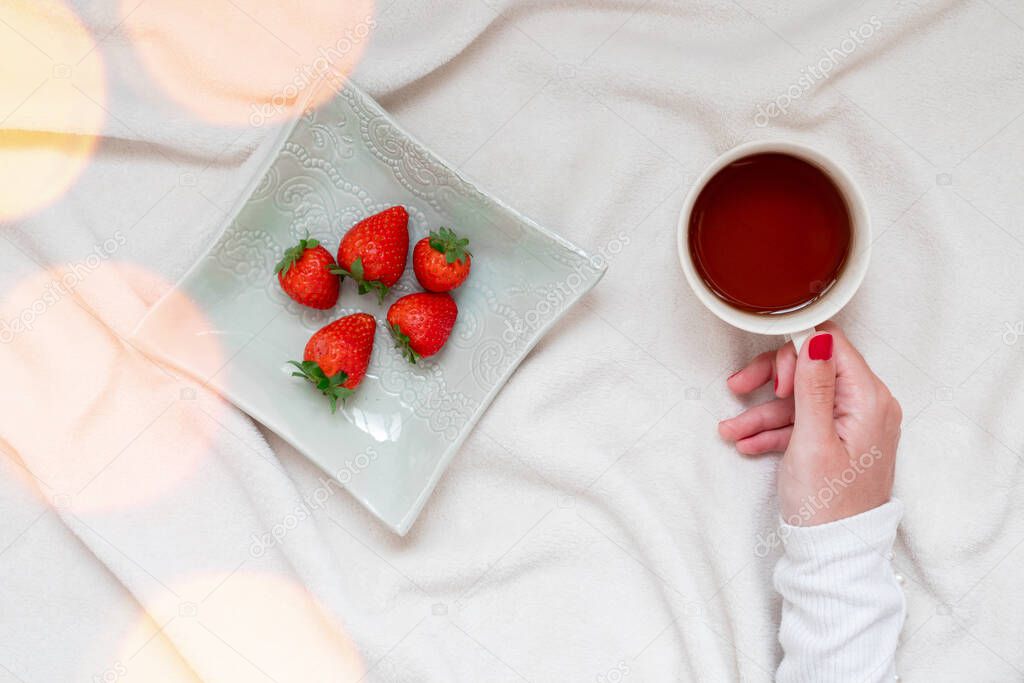 Girl holding coffee, with snack of strawberries. Cozy scene at home