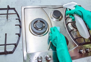 Rostoyu pişirdikten sonra fırını yıkamak, sprey ve süngerde deterjan kullanmak, açık yeşil eldivenli eller.