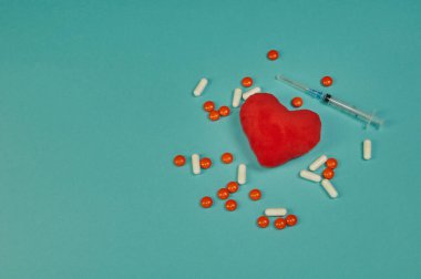 Oyuncak kırmızı kalp, turuncu tabletler, beyaz kapsüller ve tek kullanımlık şırınga şeklinde yumuşak bir oyuncak.