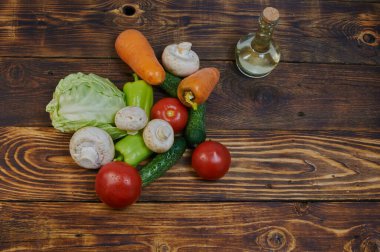 Domatesler, salatalıklar, dolmalık biberler, yarım lahana, şampiyonlar ve havuçlar ahşap bir masada ve bir sürahi zeytinyağı, üst manzara, vejetaryen yemekleri, düzgün beslenme