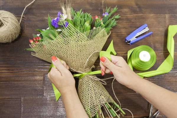 Женщина-флористка делает разноцветный букет на деревянном столе — стоковое фото