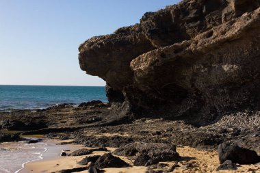 Costa Calma Beach siyah kayalar. Mavi kıyı şeridi. Playa Barca, Fuerteventura, Kanarya Adaları, İspanya. Istmo de la pared görünümü