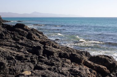 Costa Calma Beach siyah kayalar. Mavi kıyı şeridi. Playa Barca, Fuerteventura, Kanarya Adaları, İspanya. Istmo de la pared görünümü