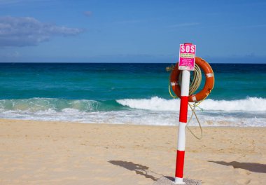 Yüzme daire. Hayat şamandıra kırmızı rengi parlak kum ve gökyüzü arka plan ile sahilde. İki uyarı işaretleri. Güvenlik görevlisi, lifebuoy, cankurtaran. Okyanus tatil.