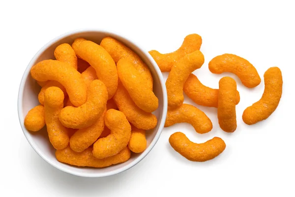 Extruded cheese puffs in a white ceramic bowl next to spilled ch — Stock Photo, Image