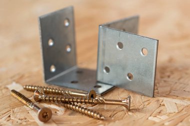 Two galvanized angle brackets and self drilling screws lying on  clipart