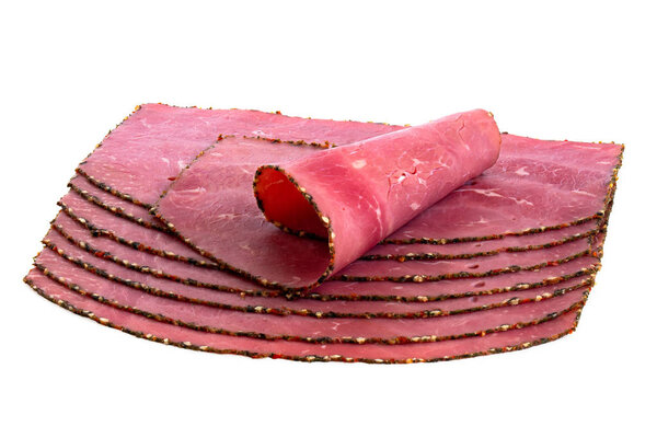A rolled slice of pastrami on top of arranged slices of pastrami isolated on white.