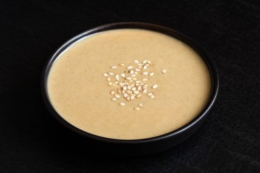 Siyah seramik bir kasede siyah üzerine susam tohumları serpiştirilmiş Tahini..