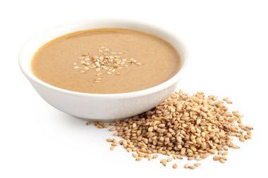 Tahini beyaz seramik bir kasede susam tohumları serpiştirilmiş beyaz üzerine izole edilmiş susam tohumlarının yanında..