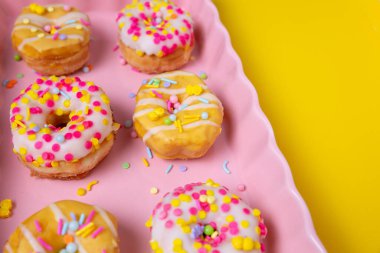 Renkli bir arka planda pembe servis tepsisine serpiştirilmiş mini çörekler.