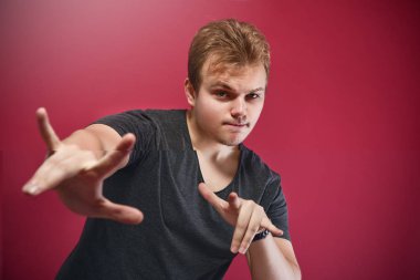 İzole edilmiş pembe arka plan üzerinde gri tişört giyen, elleri havada rock sembolü yapan genç, şık, acınası bir çocuk. Müzik yıldızı. İmzala. havalı işaret