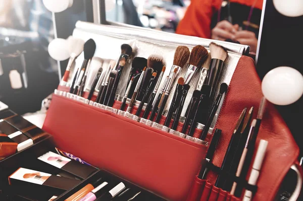 Closeup of makeup tools. Professional makeup brushes in tube, leather bag on a wooden table. Set of different objects for makeup artist in their holder. cosmetics store