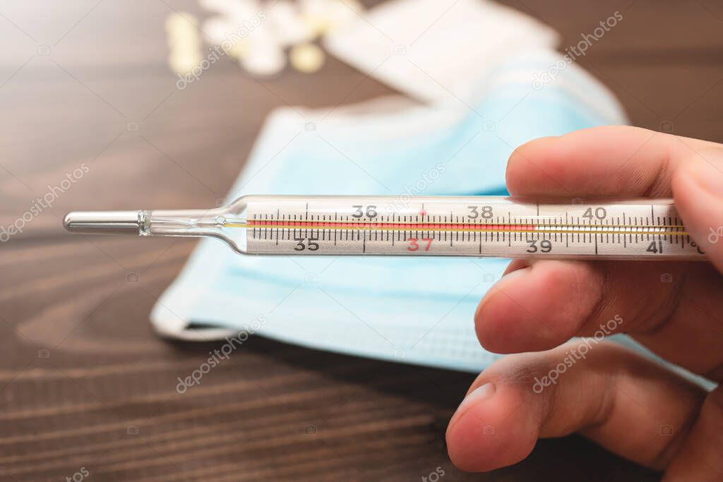 A medical clinical mercury thermometer in person's hand showing the temperature of 39 C. High temperature. wooden background. Theme of health care, medical treatment and disease prevention.