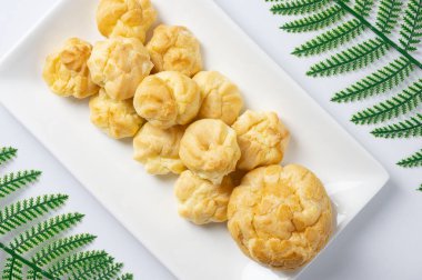 Lezzetli eklerleri ya da kremalı pufları ya da Fransız profiterollerini ya da vanilyalı kremayla doldurulmuş choux hamurunu beyaz tabağa koy. en üstteki görünüm.