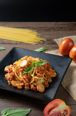 Domates soslu spagetti bolonez, ahşap arka planda siyah tabakta sosis ve fesleğen..