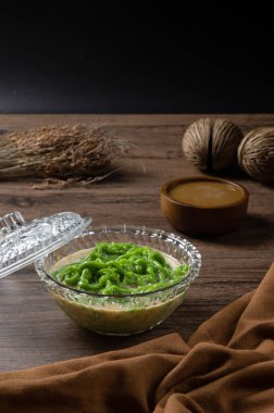 Lod Chong ya da Cendol tatlısı, pilav ve pandandan yapılan ve hindistan cevizi sütü ve palmiye şekeri şurubuyla yenen erişteye benzer şekerlemeler. ahşap arkaplanda.