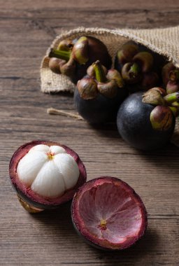 Olgun mangosteen meyveleri ve enine kesiti, kalın menekşe derisi ve beyaz eti, tahta arka planda meyve kraliçesi.