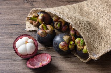 Olgun mangosteen meyveleri ve enine kesiti, kalın menekşe derisi ve beyaz eti, tahta arka planda meyve kraliçesi.