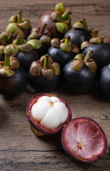 olgun mangosteen meyveleri ve kesitleri kalın menekşe derisi ve beyaz eti gösteriyor, tahta arka planda meyvelerin kraliçesi.