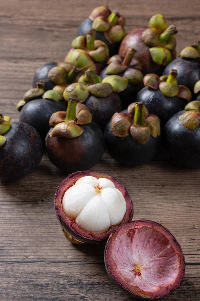 ripe mangosteen fruits and cross section showing the thick violet skin and white flesh, Queen of fruit on wooden background.