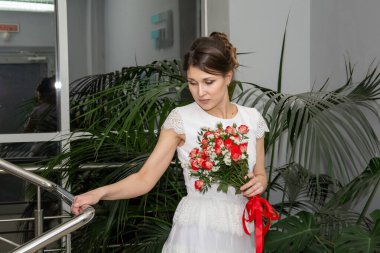 Yeşil bitkilerin arka planında bir buket çiçekli beyaz elbiseli gelin.