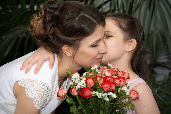 花の花束を持つ白いドレスの花嫁は 緑の植物の背景にピンクのドレスで彼女の娘を包含します — ストック写真