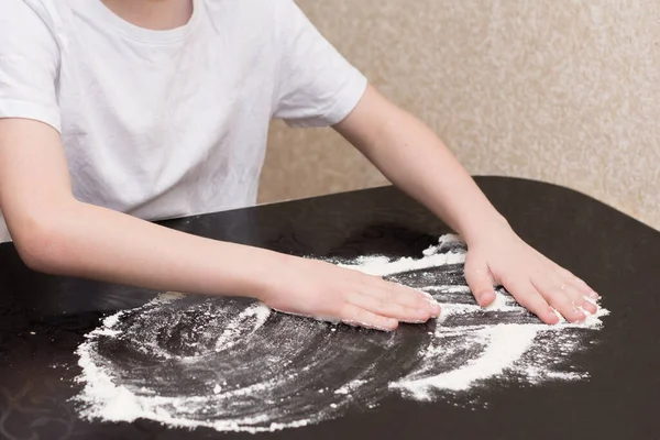 キッチンの白いTシャツに身を包んだ少年7歳ピザの準備テーブルの上に小麦粉を振りかける — ストック写真