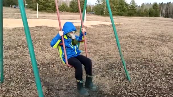 青いジャケットとガスマスクの12 13歳の少年は 隔離のために遊び場だけでスイングに乗る スローモ — ストック動画