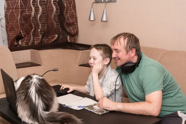 Dad and son  watches an e-learning video with a teacher on a computer in the living room of the house. E-learning, online education and online social distancing protection from COVID-19 viruses.