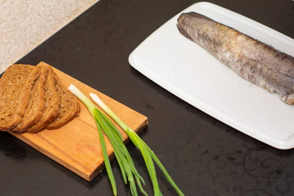 Ciemny chleb i zielona cebula są na tablicy. który leży na ciemnym stole, na stole jest oczyszczona padlina rybna. — Zdjęcie stockowe