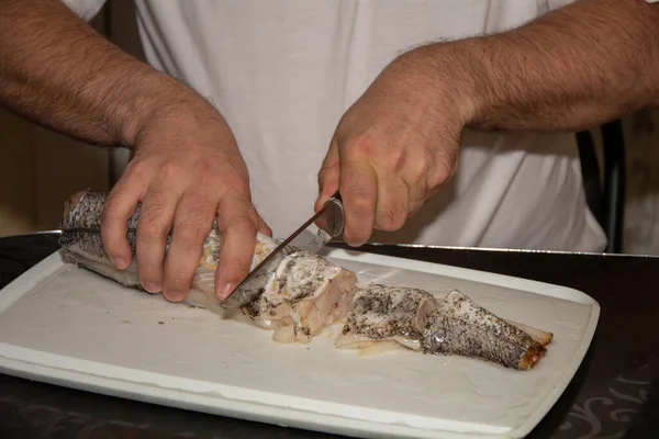 Un uomo con una maglietta bianca taglia il pesce. Pane nero fatto con farina grossolana e cipolle verdi. Natura morta in cucina Consiglio. Cibo abbondante per le regioni fredde . — Foto Stock