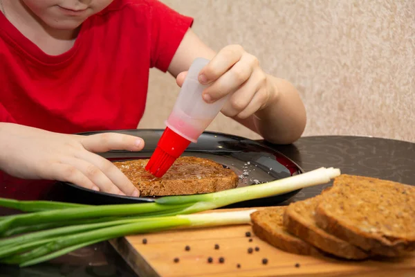Un niño de 7 años con una camiseta roja prepara un sándwich con poca sal y pan . — Foto de Stock