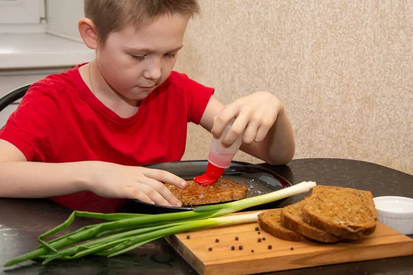 Un niño de 7 años con una camiseta roja prepara un sándwich con poca sal y pan . — Foto de Stock