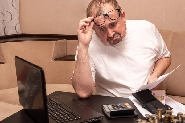 Beyaz tişörtlü ve gözlüklü sakallı bir adam aile bütçesini sayıyor, hayal kırıklığı içinde apartman faturalarına bakıyor..