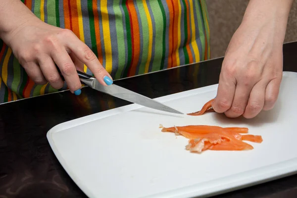 Primer plano manos chica es cortar salmones en tiras en un whiteBoard en la mesa negra . — Foto de Stock