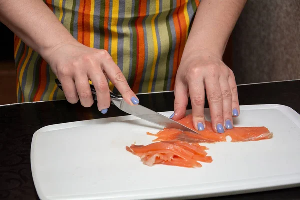 Primer plano manos chica es cortar salmones en tiras en un whiteBoard en la mesa negra . — Foto de Stock