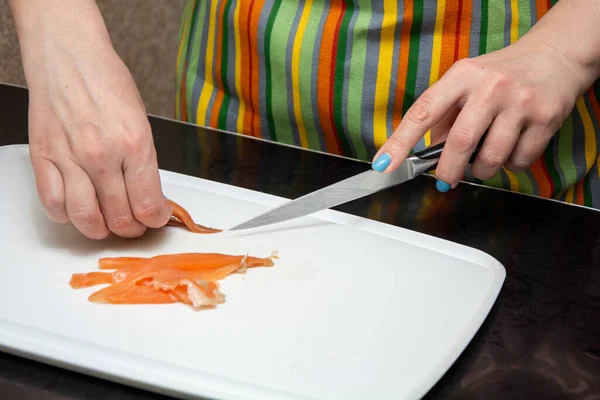 Primer plano manos chica es zurdo es cortar salmones en tiras en una pizarra blanca en la mesa negra . — Foto de Stock