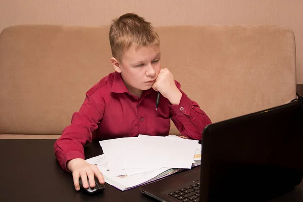 Egy piros inges fiú ül egy fekete asztalnál és házi feladatot csinál, egy gyerek karanténban a távoktatásban. — Stock Fotó