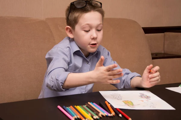 Een 6-7 jarige jongen tekent terwijl hij aan een zwarte tafel zit. Het kind tekent met gekleurde potloden. — Stockfoto