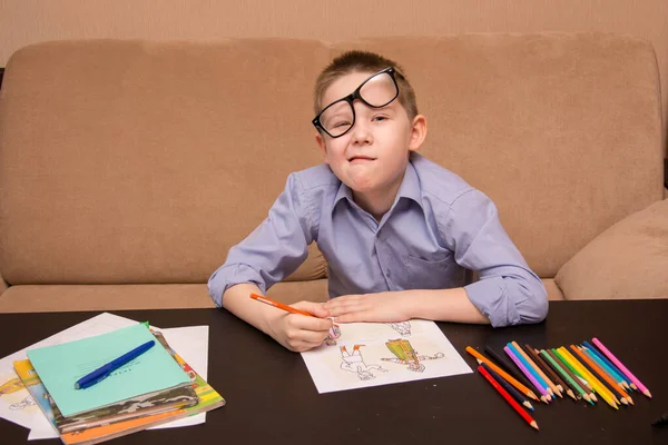 Um menino de 6-7 anos de idade com óculos desenha enquanto está sentado em uma mesa preta. A criança desenha com lápis coloridos . — Fotografia de Stock