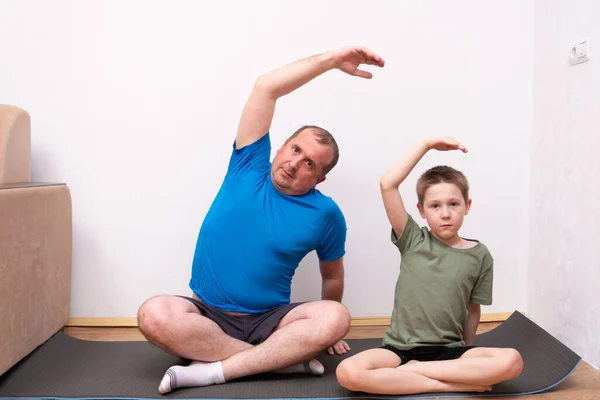 Father and son sit at home on the floor on a fitness Mat and do yoga relax. home fitness training, independent work.
