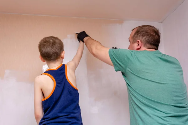 Happy father and son paint the wall white. Family values, relationships in the family