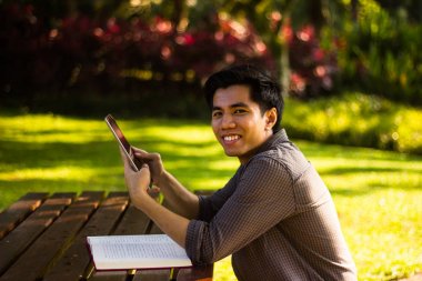 Gülümseyen genç Malay adam akıllı telefon oturma sırasında kullanarak closeup çekim