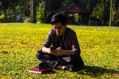 Genç Malay adam onun smartphone Park'taki kullanarak müzik dinlemek zevk